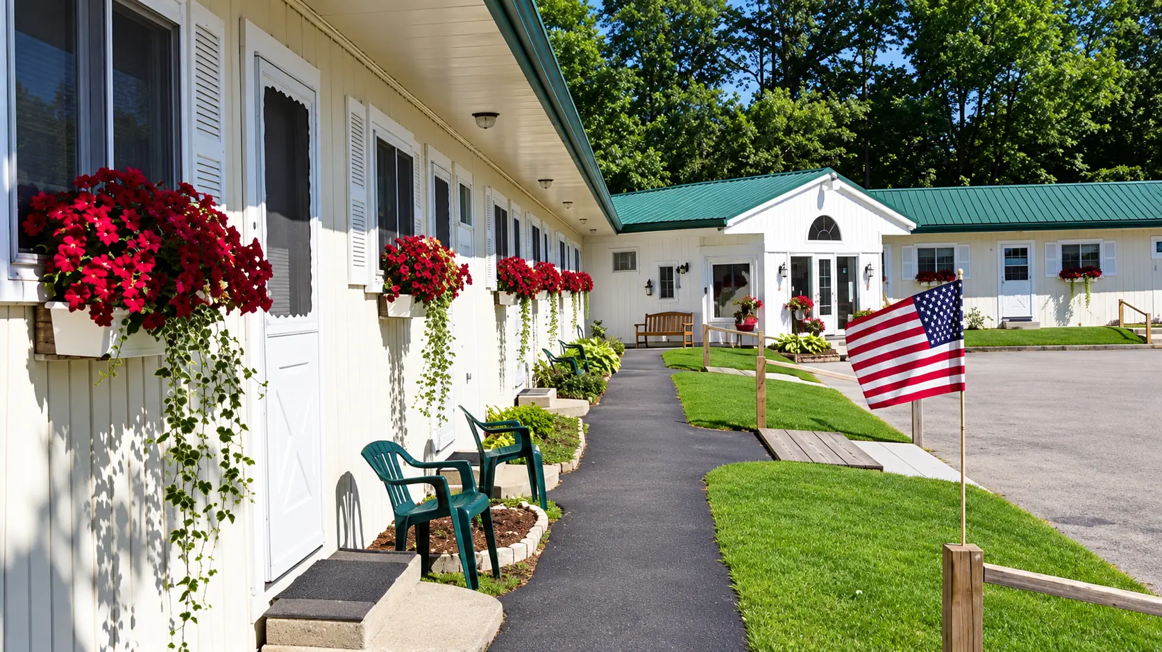 The Cobbossee Motel on a summer day: white guest rooms with red flower boxes along a paved walkway, and the green-roofed front office beyond the lawn.